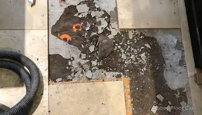 Unstable screed visible beneath a damaged travertine tile once it had been lifted.