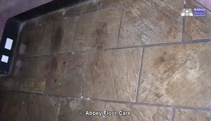 Indoor sandstone floor with a riven surface showing ingrained dirt and uneven colour.