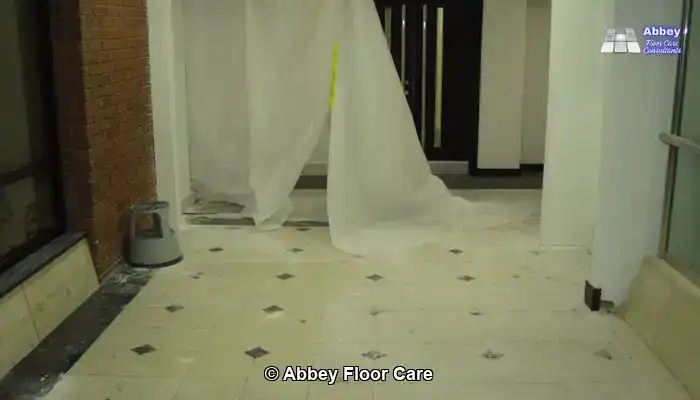 Marble tiles with adhesive patches and fine scratches revealed after carpet tiles were removed.