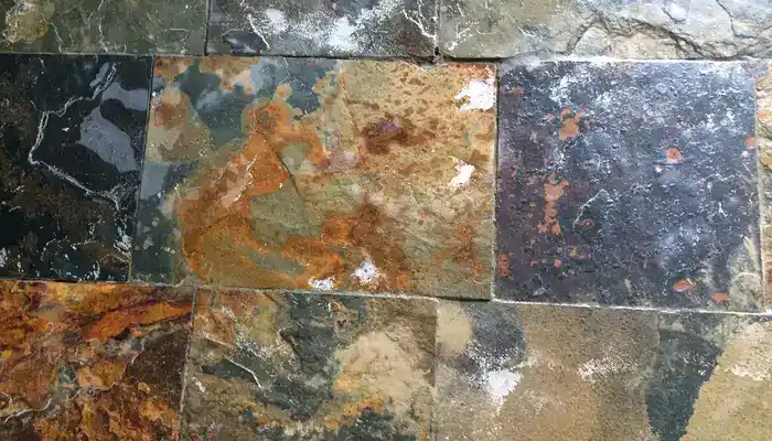 Slate floor showing surface wear, dark grout lines, and ageing across different areas.