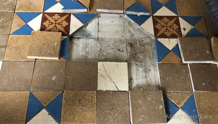 Lifted Victorian tile revealing a fractured brittle cement screed and bedding layer
